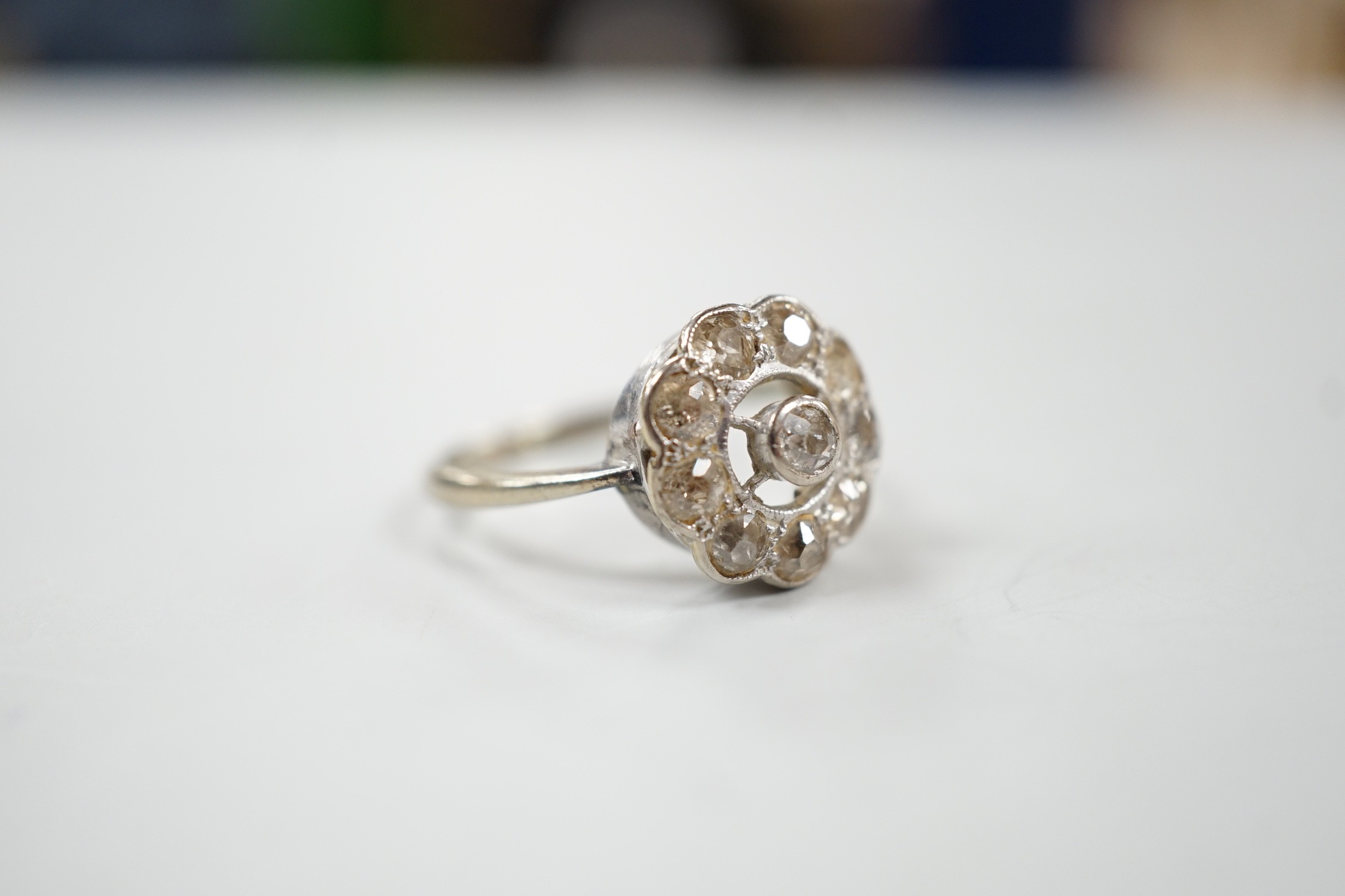 A 1920's white metal and ten stone millegrain set diamond flower head cluster ring, size P/Q, gross weight 3 grams.